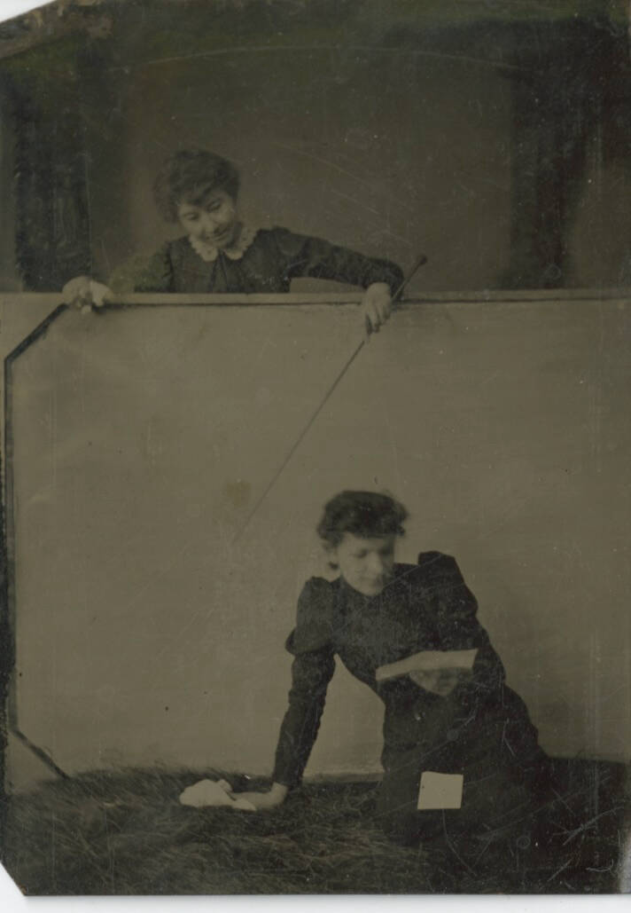 Black and white tintype photograph of two women, one is reading, the other is on the other side of the wall.